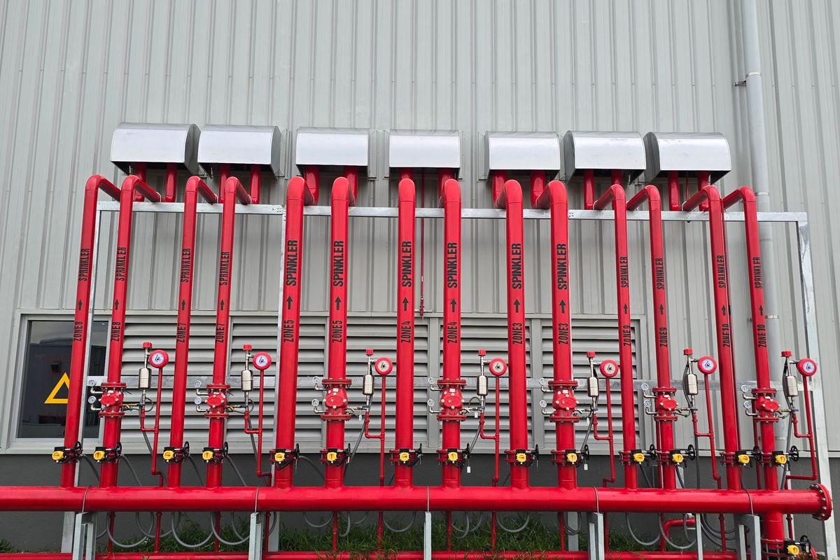 Industrial automatic fire sprinkler system riser manifold and control valves outside a modern building.