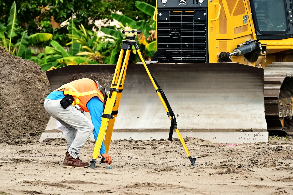Land surveyor conducting site assessment with geodetic equipment before construction