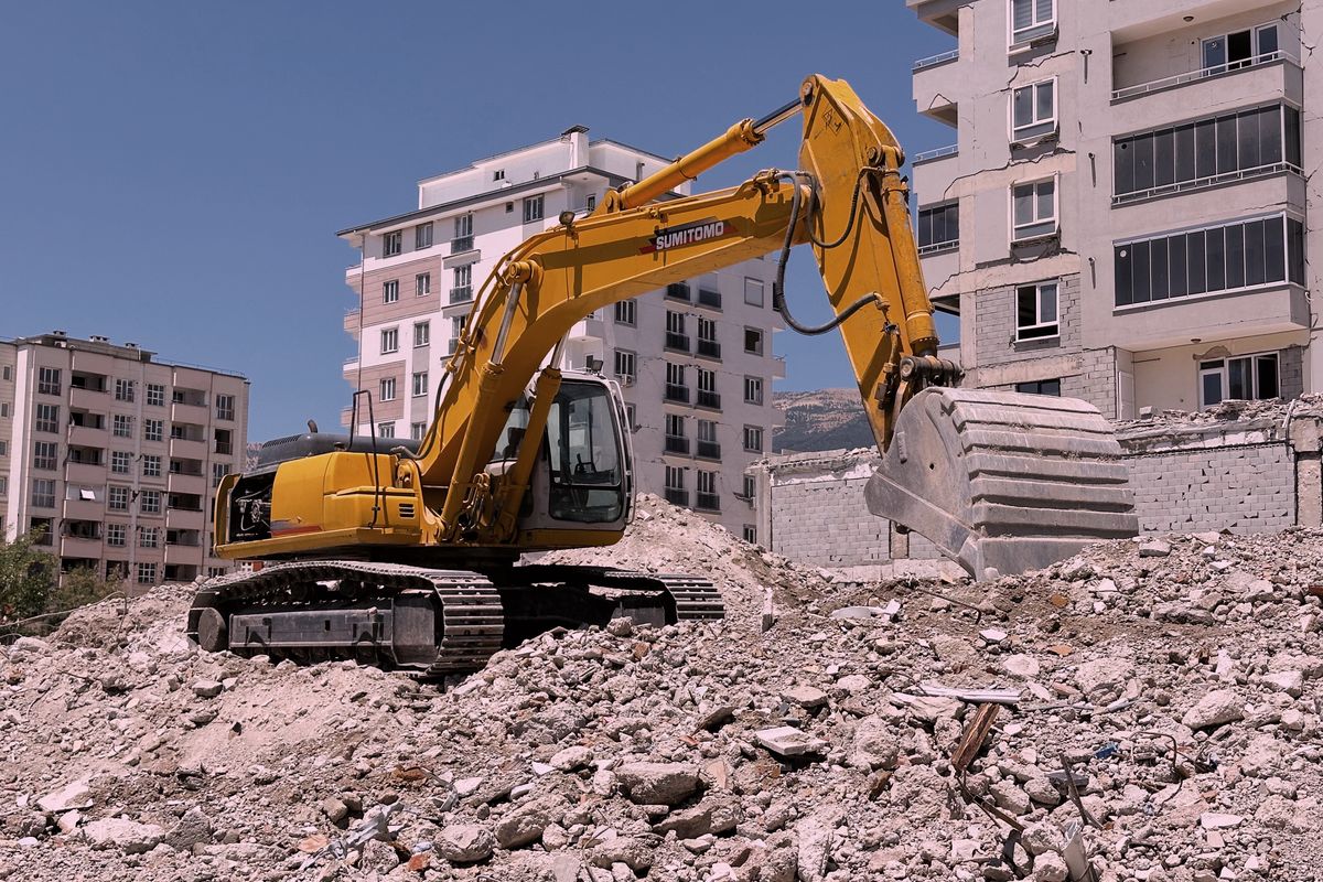 Heavy excavator clearing rubble at a residential building reconstruction site.