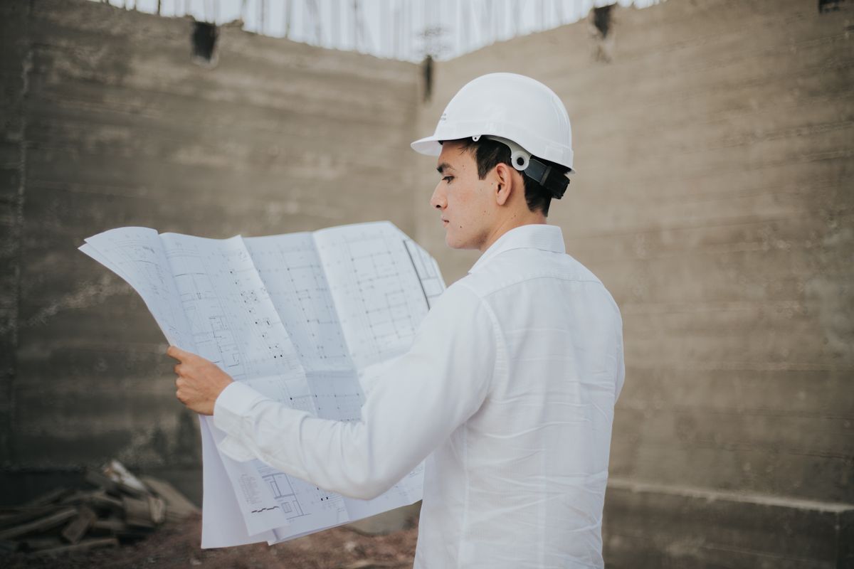 An architect in a hardhat studying blueprints at a construction site.